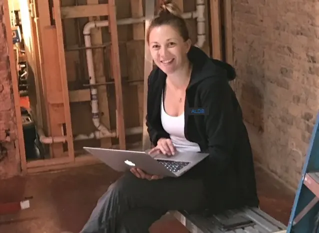 Sally Anderson Little working on a laptop at a gutted job site